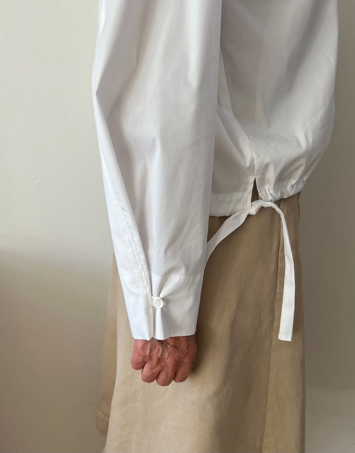 Shirt blouse in white cotton poplin seen from the side . Pull in strings and wide sleeves